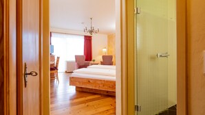 Habitación de hotel con piso de madera, una cama, un escritorio con silla, un candelabro y una puerta.