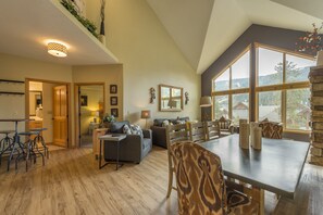 A spacious living area with a high ceiling, a dining table with chairs, and a view of the outdoors through large windows. - Top floor condo, mountain views, steps to village, free shuttle, 1 min to slopes (Keystone)