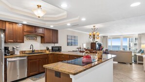 A modern kitchen with wooden cabinets, a stainless steel dishwasher, a microwave, and a large island with a kettle. - Amazing Beachfront Condo in the heart of Destin - w/FREE Beach Setup March-Oct (Destin)