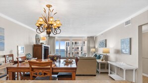 A spacious living area with a dining table, a sofa, and a chandelier. There is a view of a balcony and a pool in the background. - Amazing Beachfront Condo in the heart of Destin - w/FREE Beach Setup March-Oct (Destin)