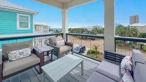 Un balcon abrité, doté d’un coin salon, d’une table et offrant une vue sur la plage et les bâtiments.