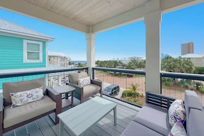 Un balcon abrité, doté d’un coin salon, d’une table et offrant une vue sur la plage et les bâtiments.