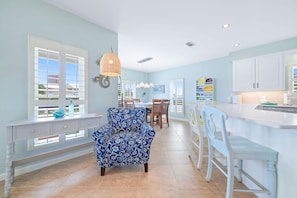 Una cocina amplia con comedor, que incluye una silla estampada en azul, armarios blancos y un ventanal grande.