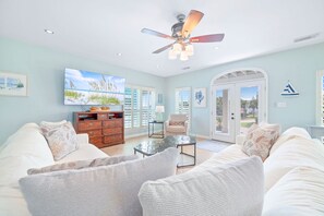 A spacious living room with a ceiling fan, a large TV, and a view of the outdoors through a sliding glass door.