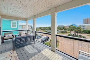 A covered balcony with outdoor furniture, a view of a residential area, and a clear sky.