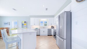 Une cuisine moderne avec des meubles blancs, un réfrigérateur en acier inoxydable et un coin repas comprenant une table et des chaises blanches.