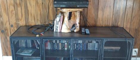 A wooden entertainment unit with a flat-screen TV mounted on top, a dog-shaped speaker, and a collection of DVDs and books.