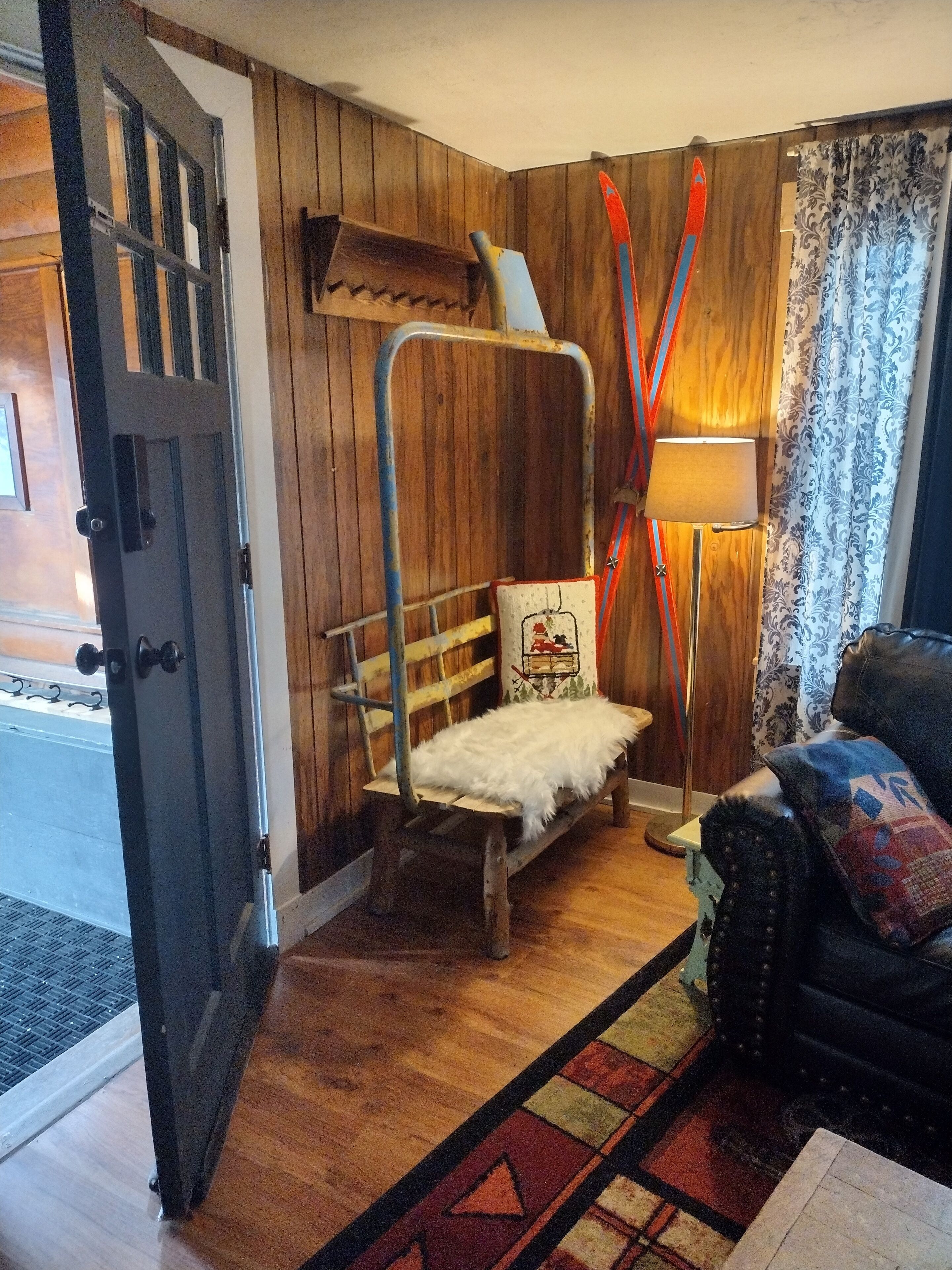 Una habitación rústica con paredes de madera, una cama litera, una lámpara y esquíes apoyados en la pared, además de una alfombra estampada.