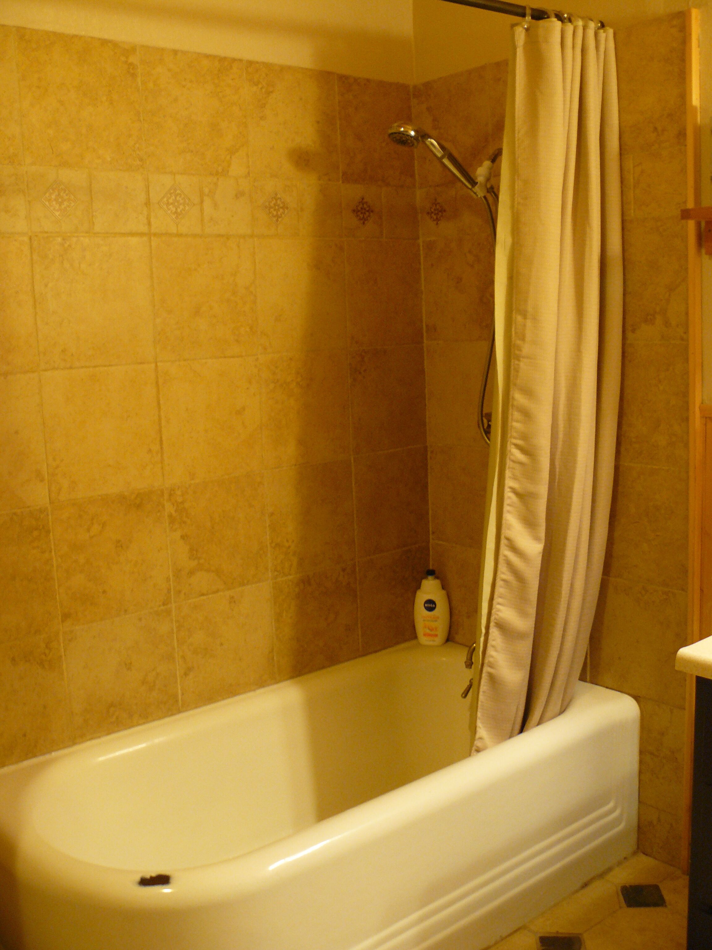 A bathroom with a bathtub, a shower curtain, and a bottle of shampoo on the floor.