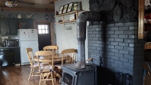 A cozy kitchen with a wood stove, wooden furniture, and a stone accent wall. - Cozy Cabin minutes from Yellowstone, fly fishing, skiing and snowmobiling.  (Island Park)