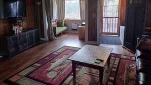 A living room with a television, sofa, and a table. - Cozy Cabin minutes from Yellowstone, fly fishing, skiing and snowmobiling.  (Island Park)