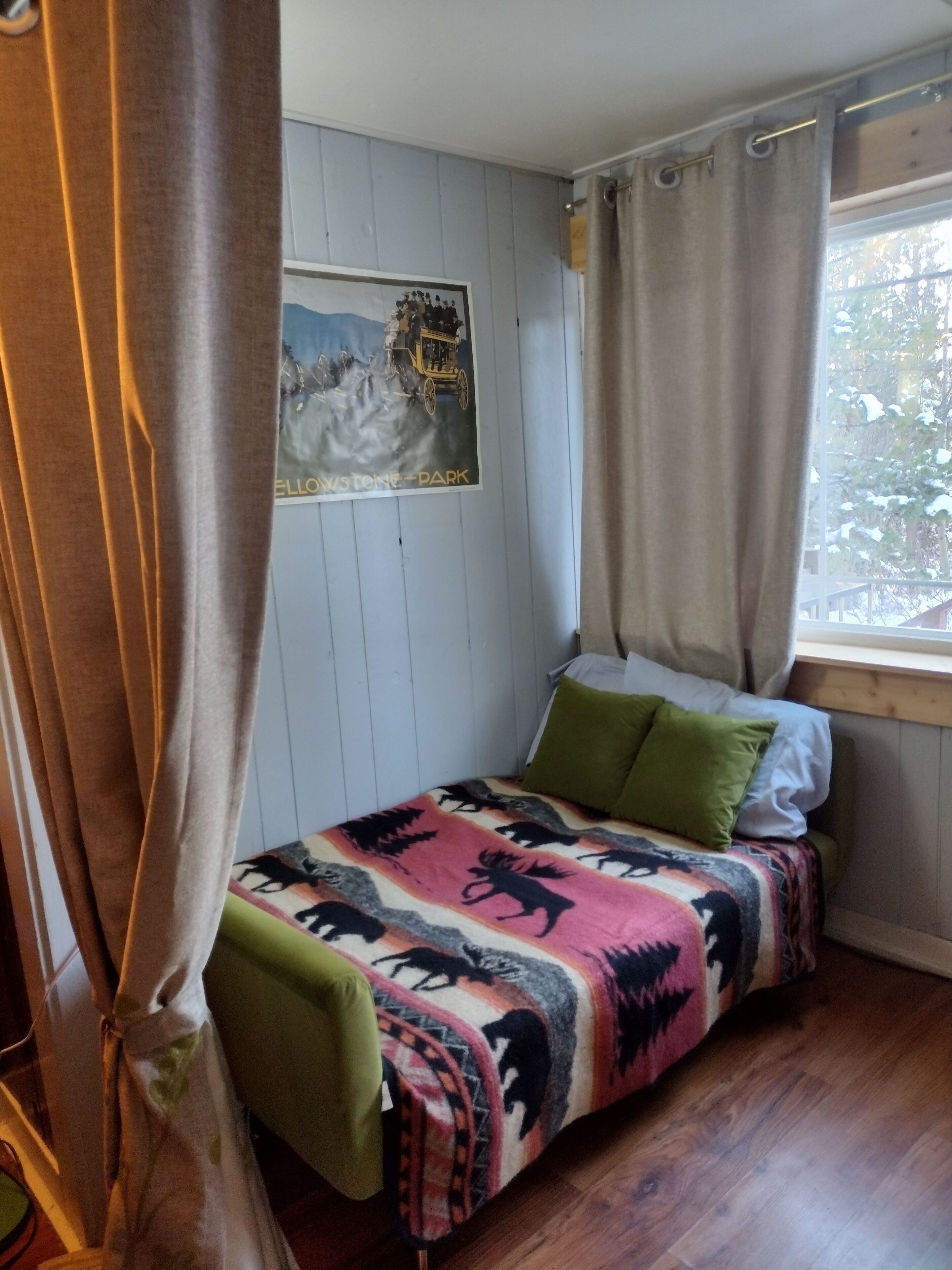 Ein Schlafzimmer mit Bett, einem fenster mit Vorhängen, einem Wandposter und Holzboden.