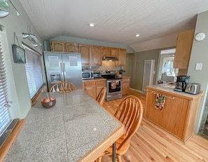A compact kitchen with wooden cabinets, a granite countertop, and a dining area with two wooden chairs.