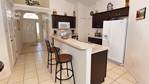 A kitchen with a central island, dark cabinets, white appliances, and a tiled floor. - Glenbrook Retreat-Come in as Guests and Leave as Friends (Clermont)