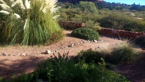 A desert landscape with a prominent red rock formation in the background, surrounded by various green shrubs and grasses. - Casa de Saltillo - single level home, gorgeous views, close to trails. (Sedona)