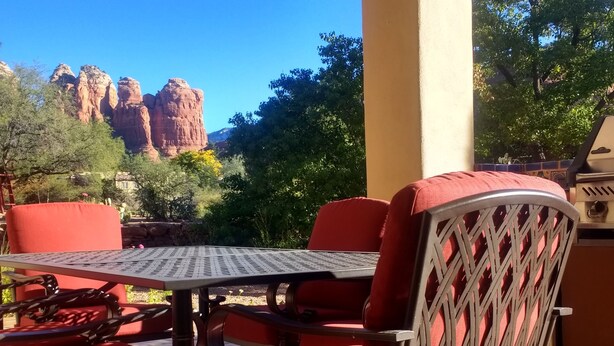 An outdoor patio with a table and red chairs, overlooking a mountainous landscape. - Casa de Saltillo - single level home, gorgeous views, close to trails. (Sedona)