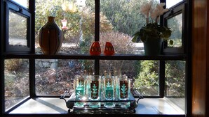 Una ventana con vistas a un jardín, un florero, una planta en maceta y una bandeja de vasos pequeños.