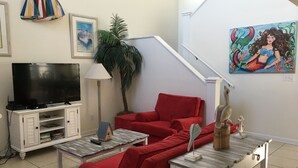 A living room with a red sofa, a TV on a white cabinet, a lamp, a plant, and a painting on the wall. - Professionally Decorated,100 Yards to Beach, Shared Pool (Surfside Beach)