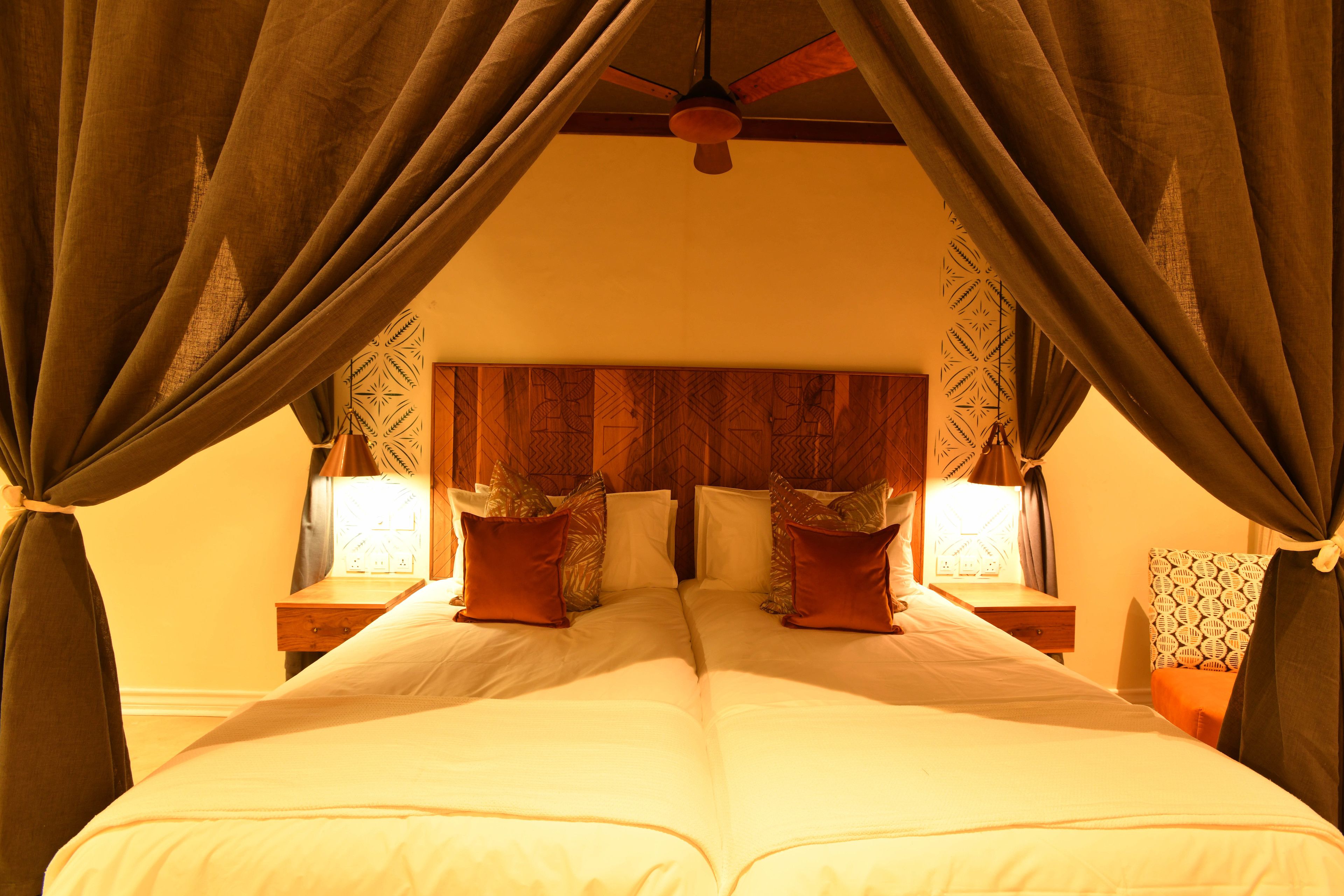 A double bed with a wooden headboard, two bedside tables with lamps, and draped curtains.