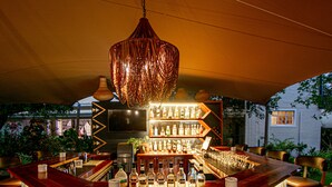 Un espace bar avec un comptoir en bois, des tabourets de bar, un luminaire suspendu et une étagère remplie de bouteilles.