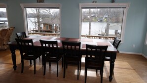 A dining area with a wooden table and chairs, large windows with a view of a lake and houses, and a 'Relax' sign on the wall. - A Second Wind! With Sliding board/diving board!! (Huddleston)