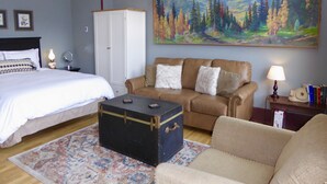 A hotel room with a bed, a sofa, a chest of drawers, a painting of a forest, and a small table with a lamp. - Studio Loft in historic Silverton Building (Silverton)