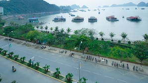 A coastal cityscape with a river, boats, and a road with parked motorcycles. - Phu Thanh Sea View Hotel (Hai Phong)