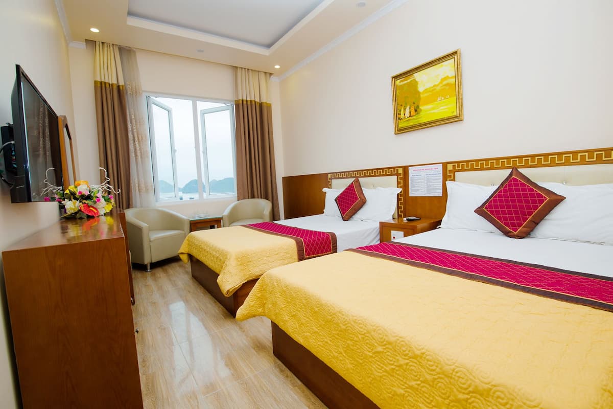 A hotel room with two beds, a desk, a TV, and a window with curtains.