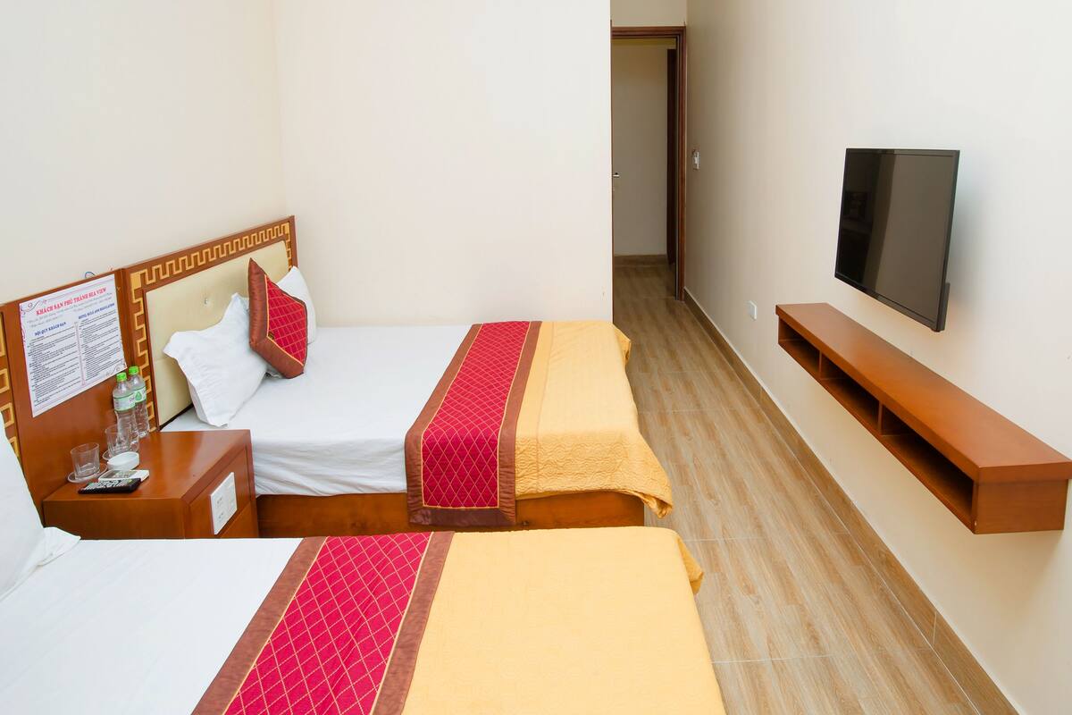 A hotel room with two beds, a TV, and a wooden bench.