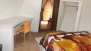 A small, well-lit room with a desk, chair, and bed. There is a door leading to another room. - Pumpkin Villa  Lombok (Senggigi)
