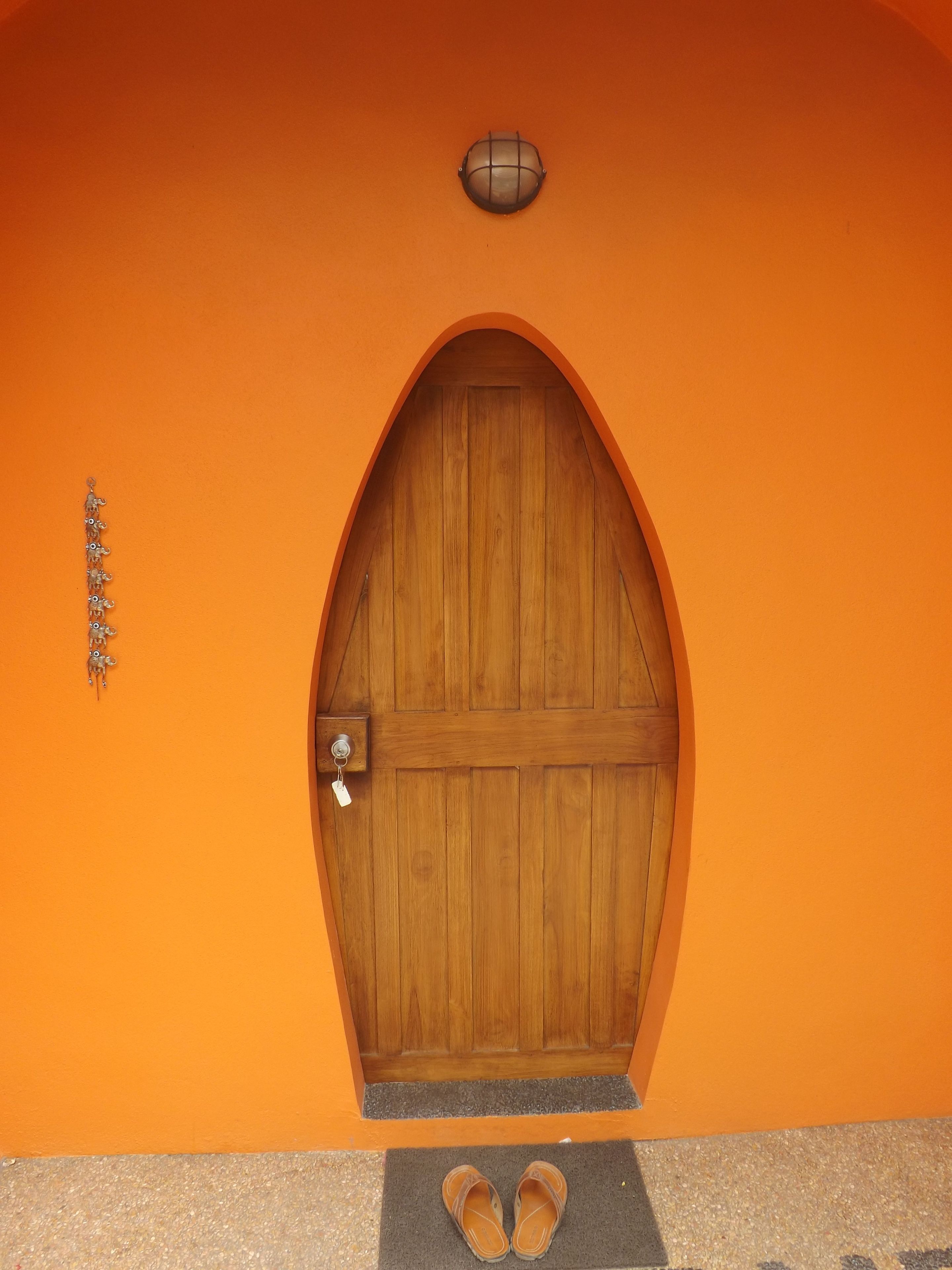 Una porta di legno con maniglia metallica e una serratura, incassata in un muro color arancione con un piccolo faretto sopra.