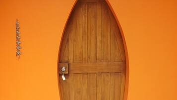 Una porta di legno con maniglia metallica e una serratura, incassata in un muro color arancione con un piccolo faretto sopra.