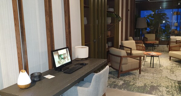 A hotel room with a desk, computer, lamp, and seating area with chairs and a sofa.