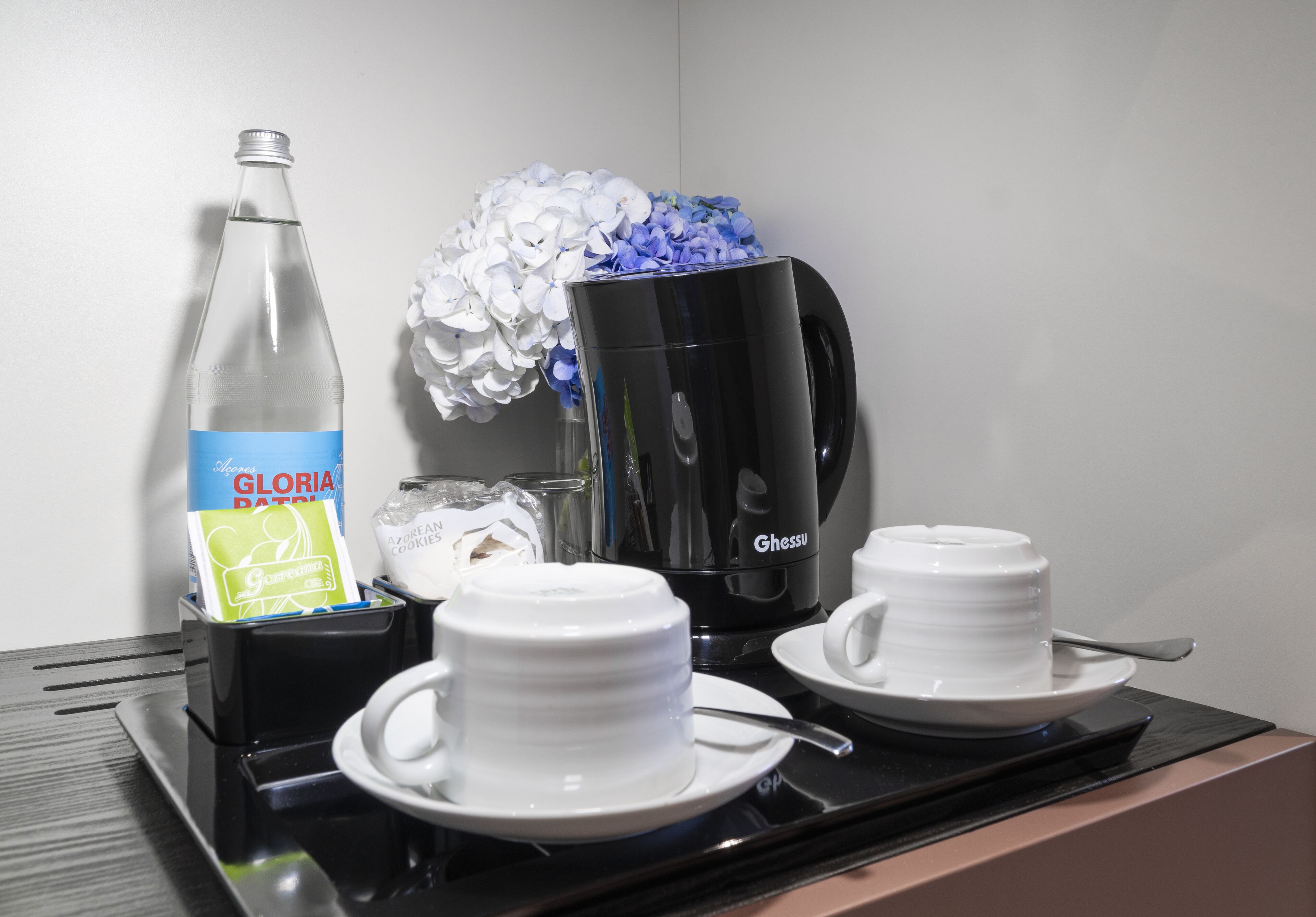 A coffee station with a coffee maker, two cups, a bottle of water, and a container of sugar.