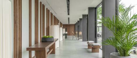 Um corredor moderno com painéis de madeira, um banco, uma planta em vaso e uma área de estar com mesa e cadeiras.