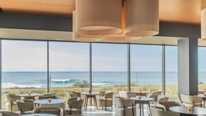Een ruime eetruimte met grote ramen met uitzicht op zee, moderne hanglampen en een strak, minimalistisch design.