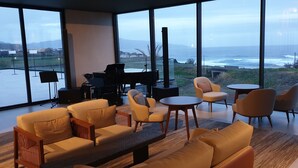 Een moderne woonkamer met een piano, banken en tafels, met uitzicht op een prachtig zeegezicht.