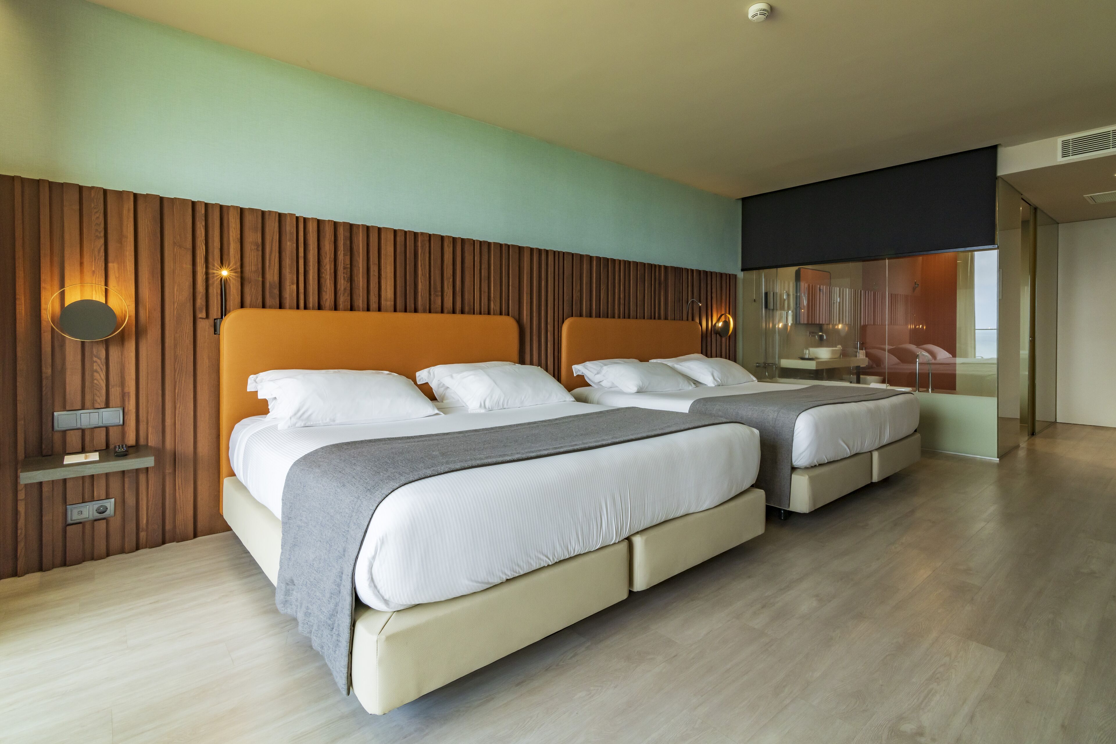 Een moderne hotelkamer met twee bedden, een houten accentmuur, een spiegel en uitzicht op de stad.