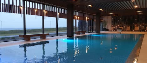 An indoor swimming pool with benches and a view of the beach.