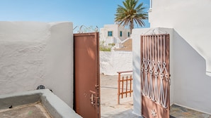 A white building with a brown door and metal gate, a stone-paved area, and a clear blue sky. - Casa La Perla (Rhodes)