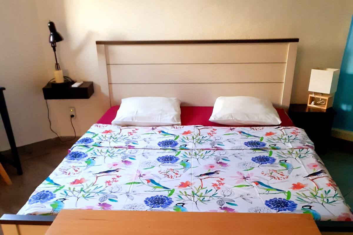 A bed with a floral bedspread, two white pillows, and a wooden bench at the foot of the bed.