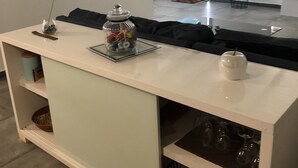 Ein modernes Wohnzimmer mit einem weißen Konsolentisch, einem Glasbehälter mit Snacks, einer weißen Tasse und einer Glasvitrine mit Weingläsern.