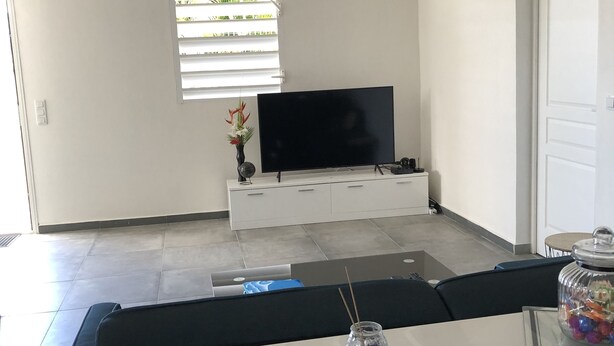 Ein modernes Wohnzimmer mit einem Flachbildfernseher, einer weißen Unterhaltungsecke, einem schwarzen Sofa und einer Glasvase mit Pflanze.