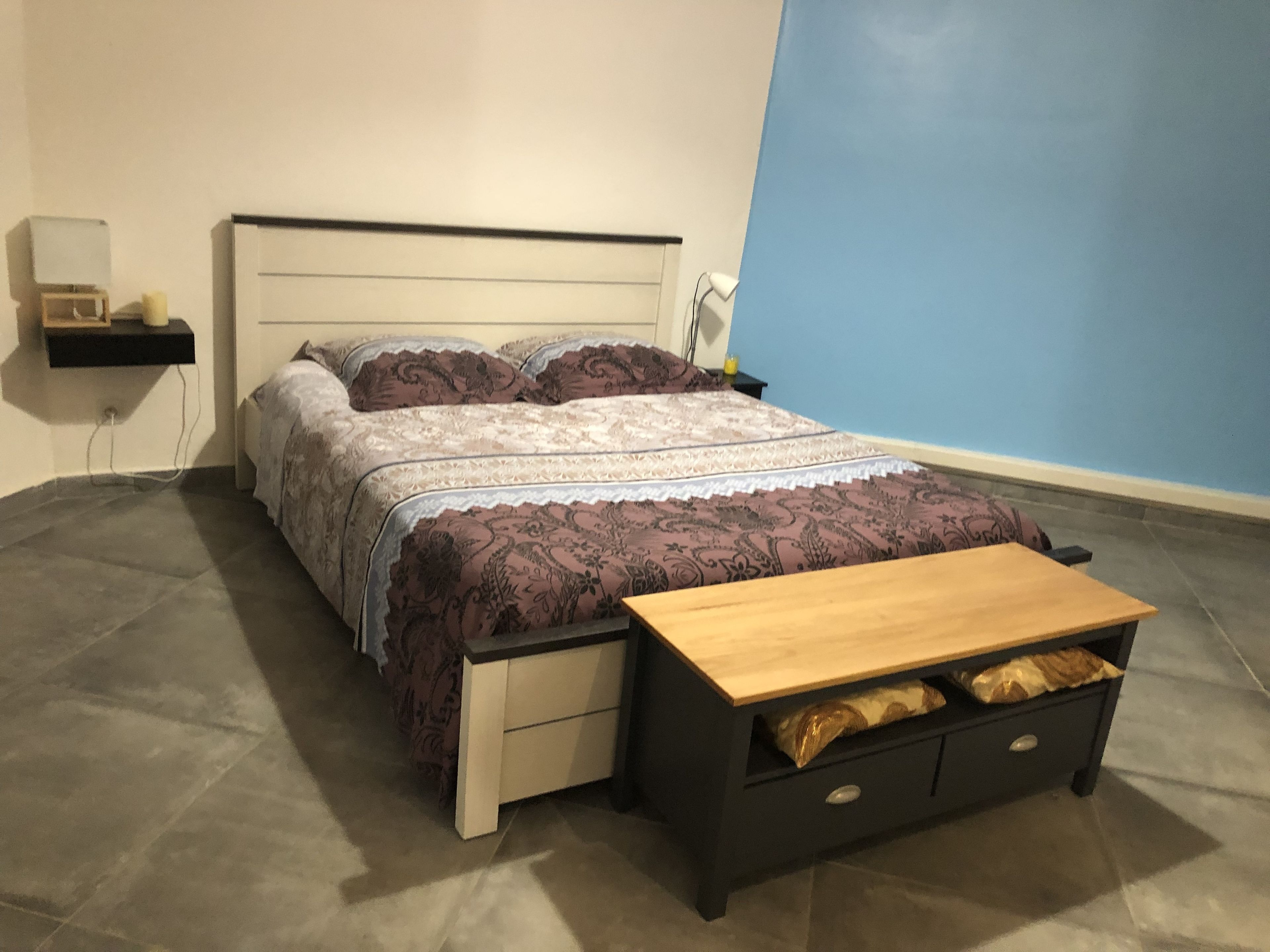 A bedroom with a bed, bedside tables, a nightstand, a lamp, and a wooden bench.
