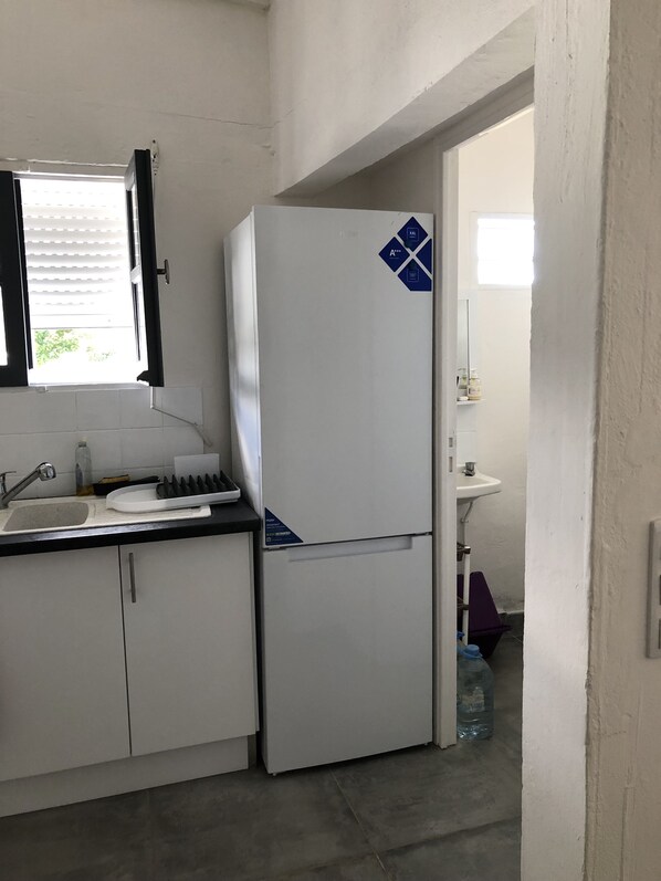 A compact kitchen with a white refrigerator, a sink, and a window with blinds.