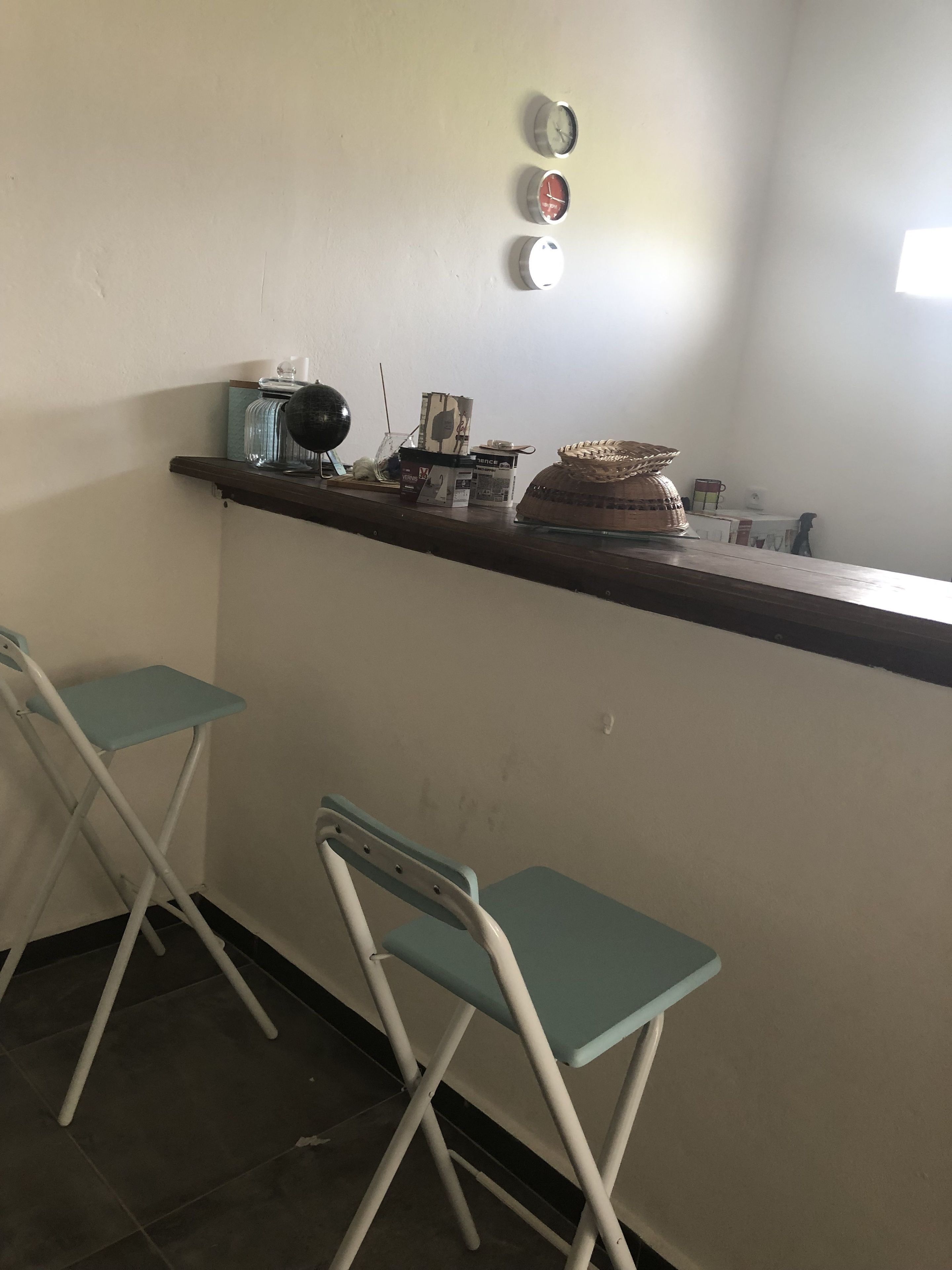 A small kitchen area with a counter, two folding chairs, and three wall clocks.