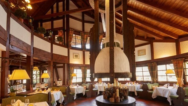 A restaurant with wooden beams, round tables, and a central decorative feature. - Kamino (Häusern)