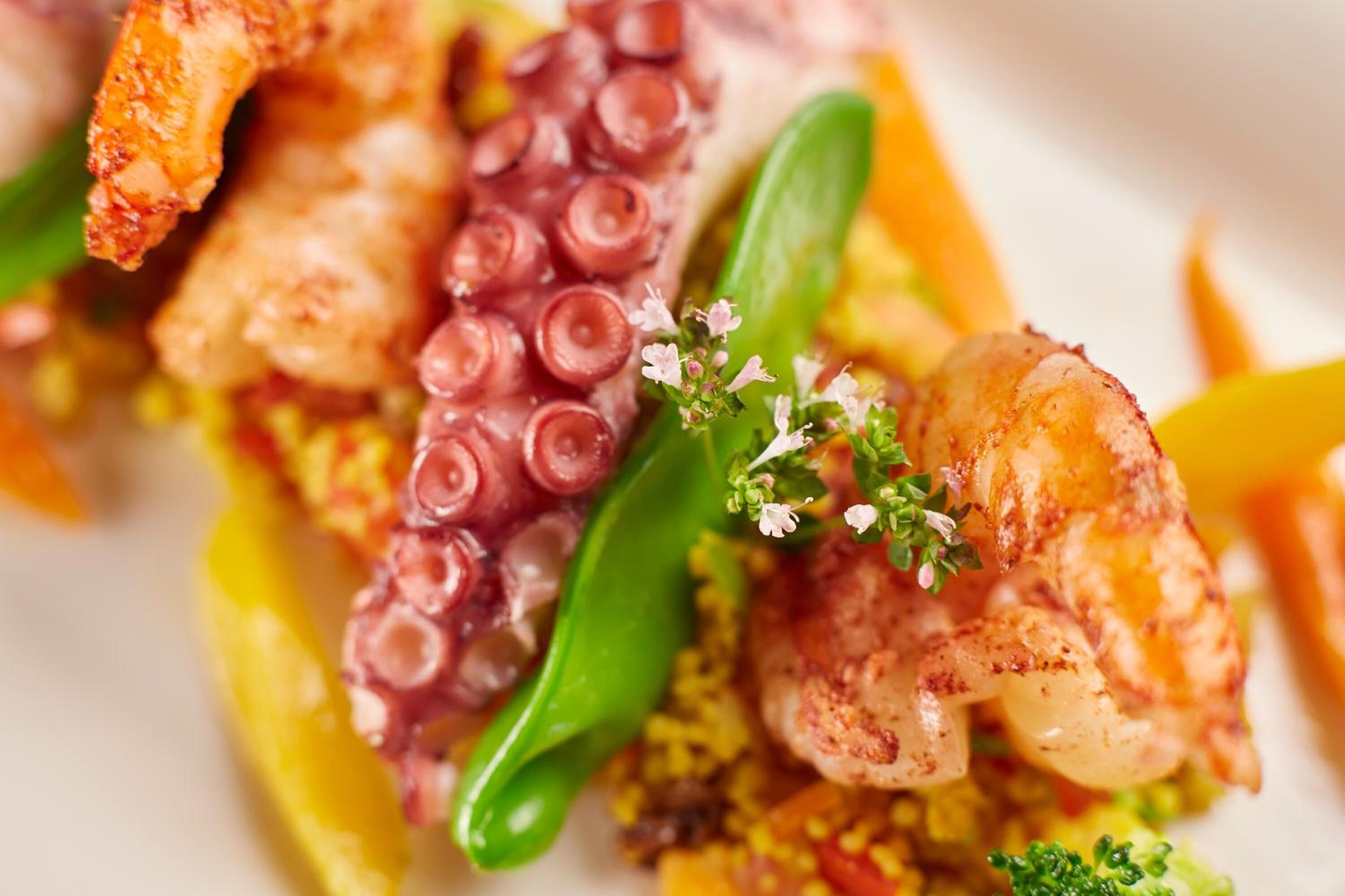A close-up of a seafood dish with octopus, shrimp, and green vegetables.