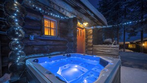 A log cabin with a hot tub outside, surrounded by snow. - Kuukkeli Hirvas Suite (Saariselka)