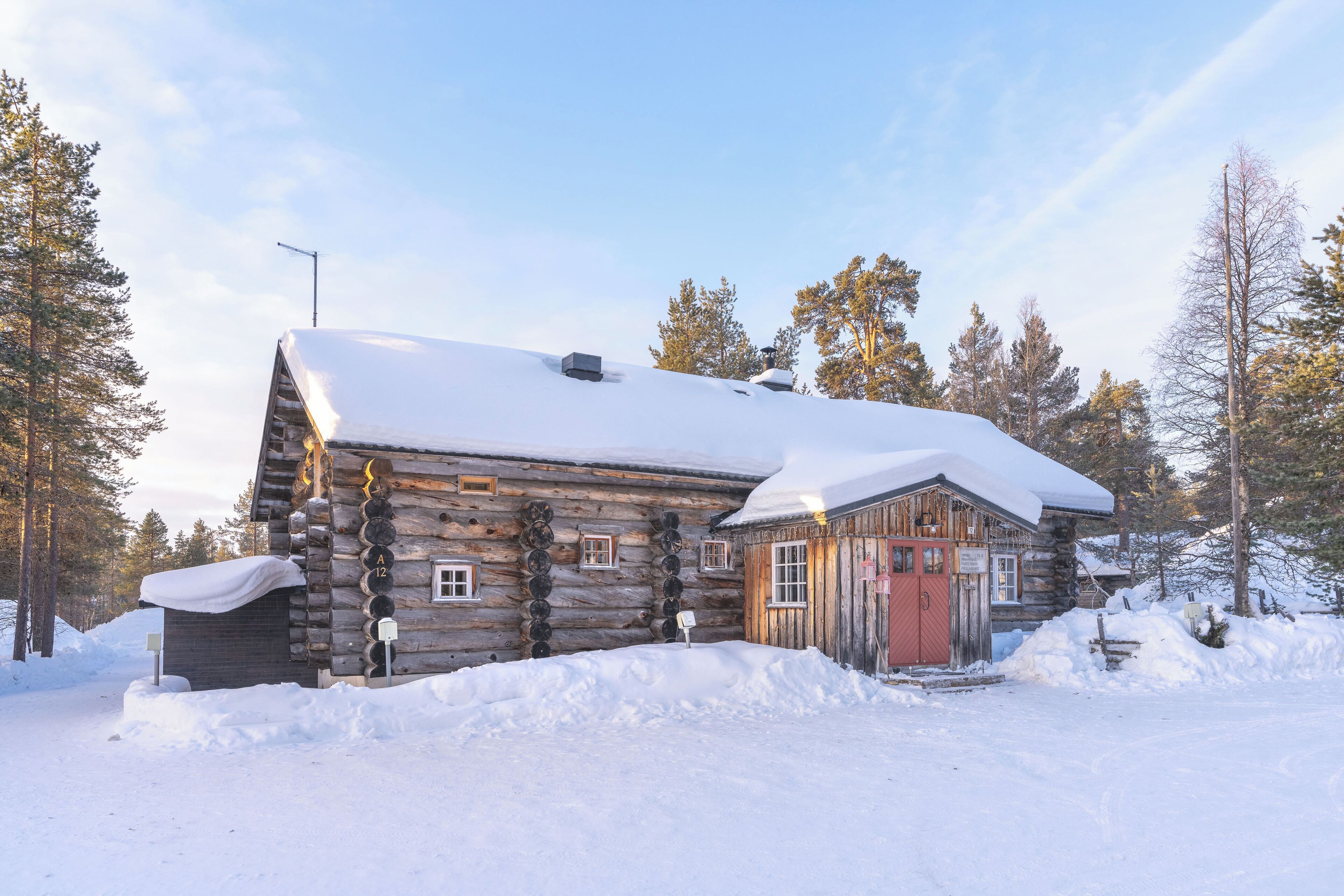Une cabane en rondins dont le toit est recouvert de neige, entourée d’arbres.